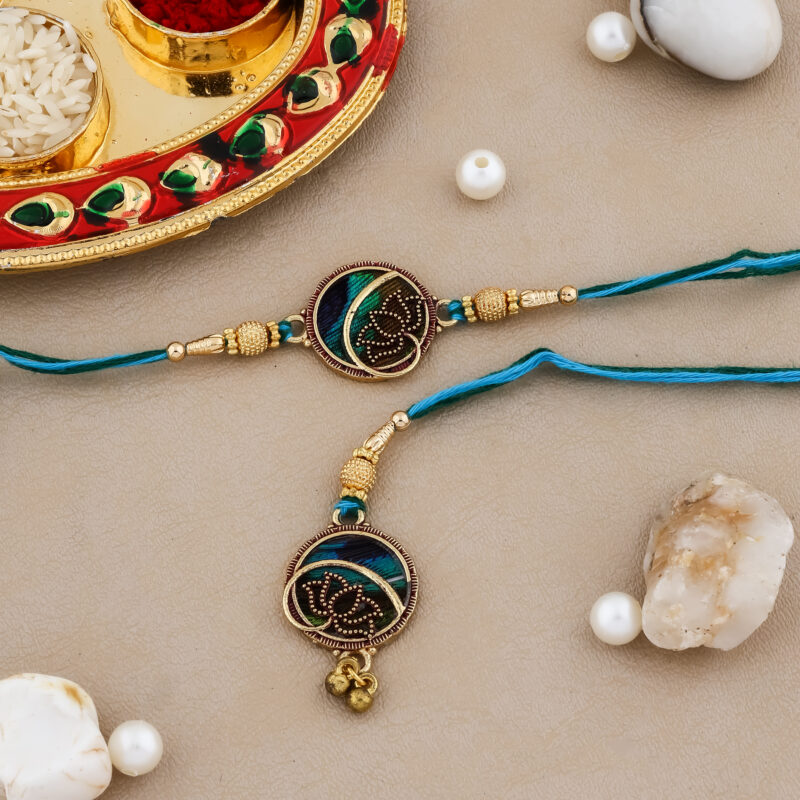 Ethnic-style Bhaiya-Bhabhi Rakhi set with blue-green thread, round golden centerpiece, traditional kumkum-chawal thali, and festive decorative background.