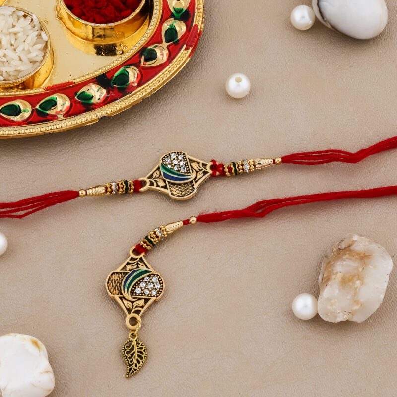 Bhaiya-Bhabhi Rakhi set with golden leaf design, red threads, stone embellishments, and a festive thali with kumkum and chawal.