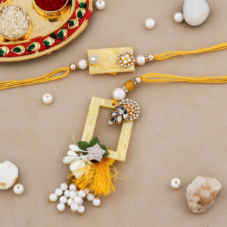 "Designer Bhaiya Bhabhi Rakhi set with pearl embellishments, kundan work, and a decorative yellow thread, accompanied by a traditional puja thali."