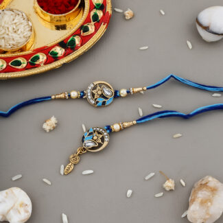 Royal-themed Bhaiya-Bhabhi Rakhi set with blue thread, crown and teardrop motif, and decorative kumkum-chawal thali with festive pearls and stones.