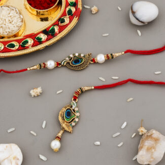 Peacock feather-themed Bhaiya-Bhabhi Rakhi set with red threads, golden detailing, pearl embellishments, and a decorative kumkum-chawal thali.